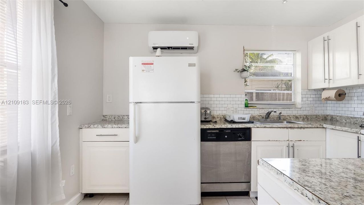 Kitchen featuring white shaker-style cabinetry, stone-finish countertops, subway tile backsplash, stainless steel dishwasher, and wall-mounted climate control unit
