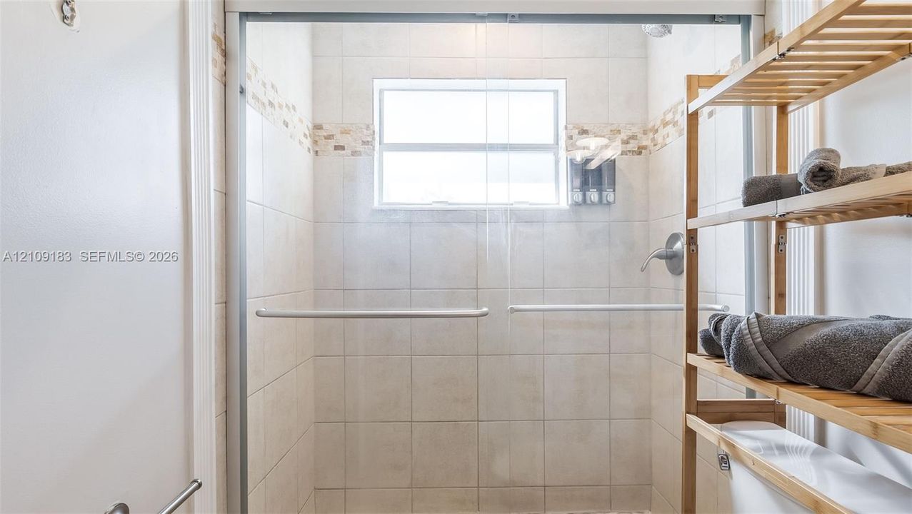 Walk-in shower enclosure featuring light-toned ceramic wall tile, horizontal mosaic tile accent banding, a framed glass door, and a built-in window