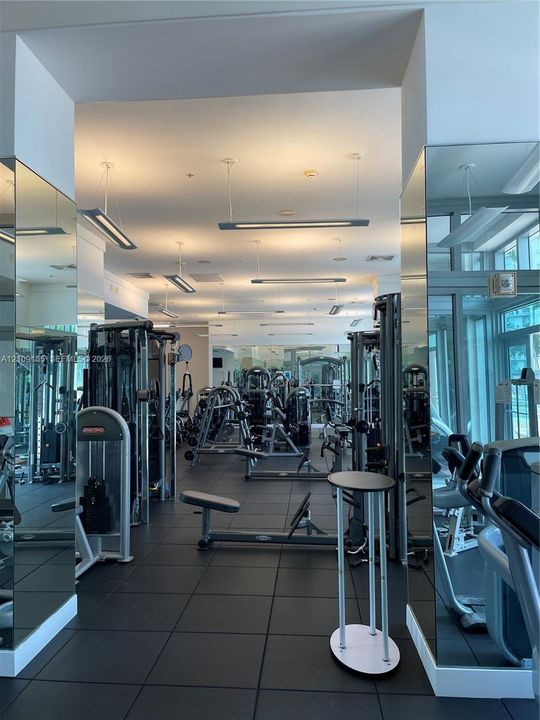 Fitness facility featuring rubberized flooring, floor-to-ceiling mirrored walls, and linear pendant lighting