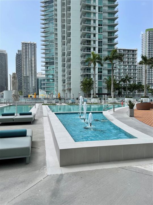Swimming pool area featuring a rectangular fountain, concrete decking, and mature palm trees