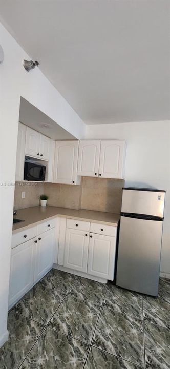 Kitchen featuring white cabinetry, solid-surface countertops, stone-patterned tile flooring, and stainless steel appliances