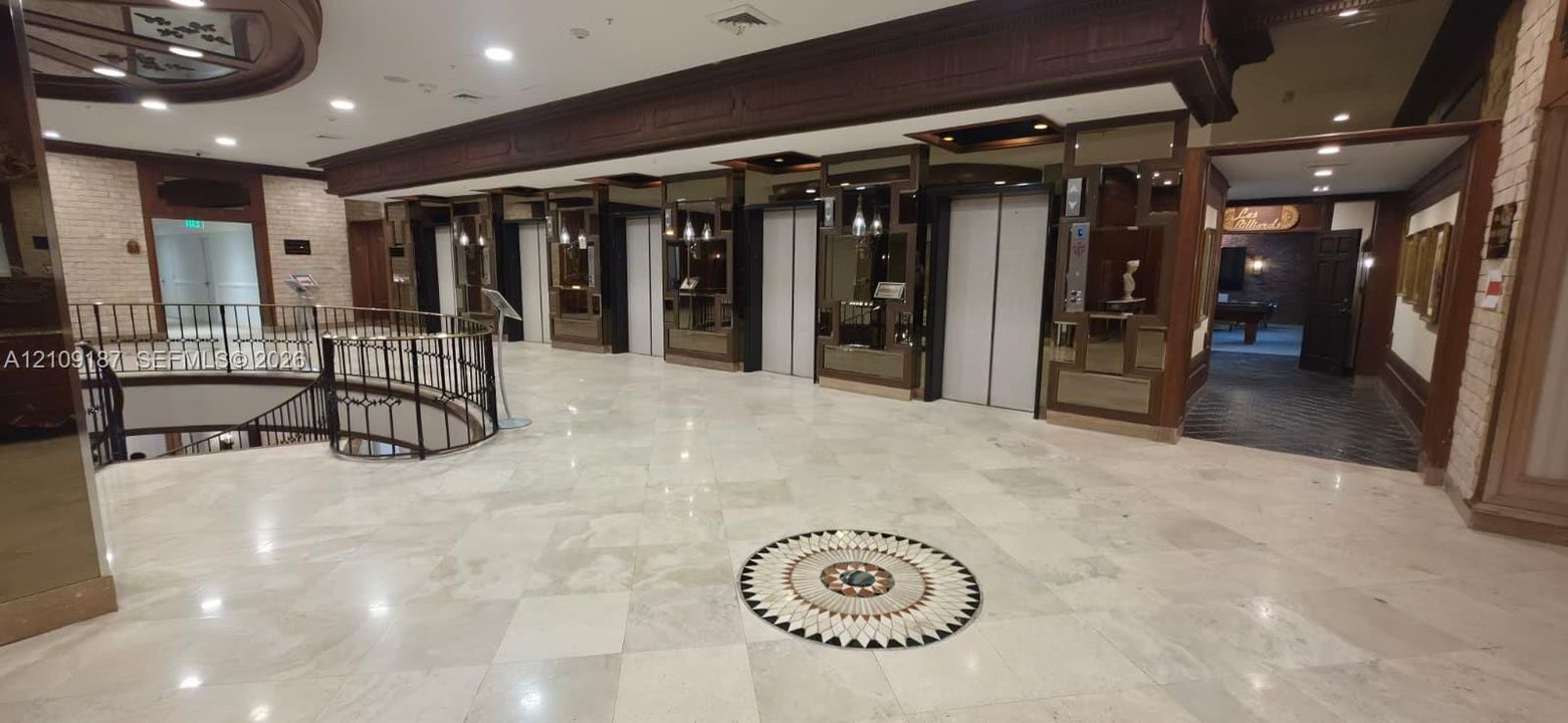 Grand lobby featuring marble flooring with decorative inlay, multi-elevator bank, ornate iron stair railing, and wood-paneled accents
