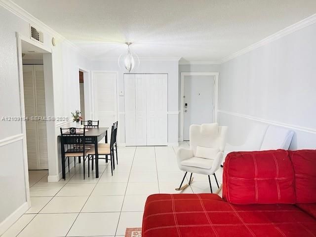 Open-concept living space featuring ceramic tile flooring, crown molding, chair rail detailing, louvered closet doors, and a contemporary spherical pendant light fixture
