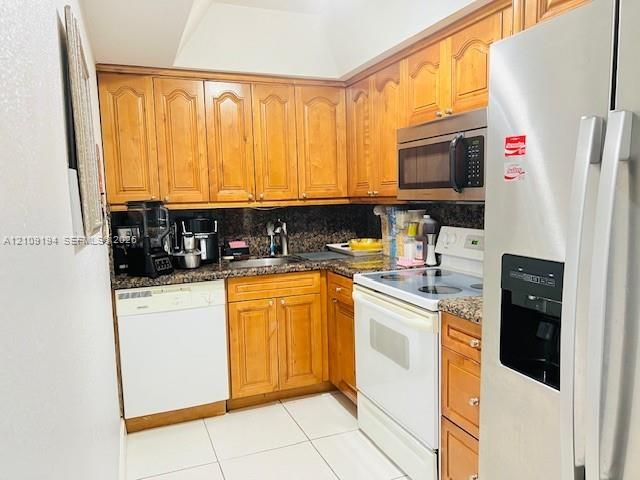 Kitchen featuring wood cabinetry, granite countertops & backsplash, and stainless steel appliances