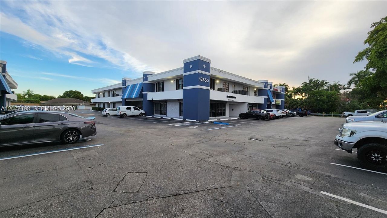 Two-story commercial building featuring blue architectural column accents, striped canvas awnings, a paved parking area, and multi-pane window glazing
