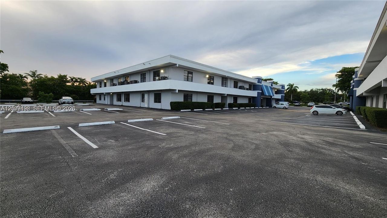 Two-story exterior featuring a flat roofline, second-level balcony, and asphalt parking area with dedicated spaces