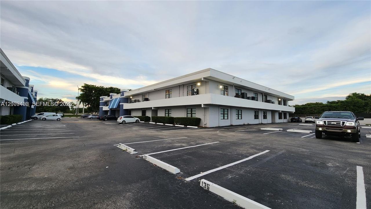 Two-story commercial exterior featuring a flat roofline, painted concrete facade, multiple windows, and a paved surface parking lot with designated spaces