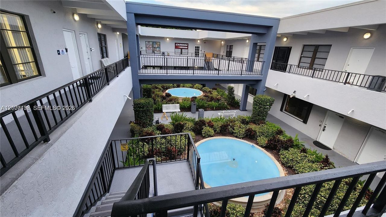 Courtyard featuring two circular water features, landscaped shrubbery, metal railings, and multi-level pedestrian walkways