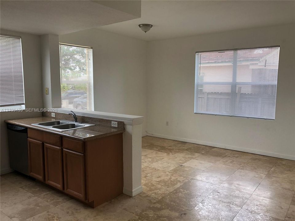 Kitchen featuring stone-finish countertops, stainless steel dual-basin sink, wood-finish cabinetry, built-in dishwasher, and large-format tile flooring