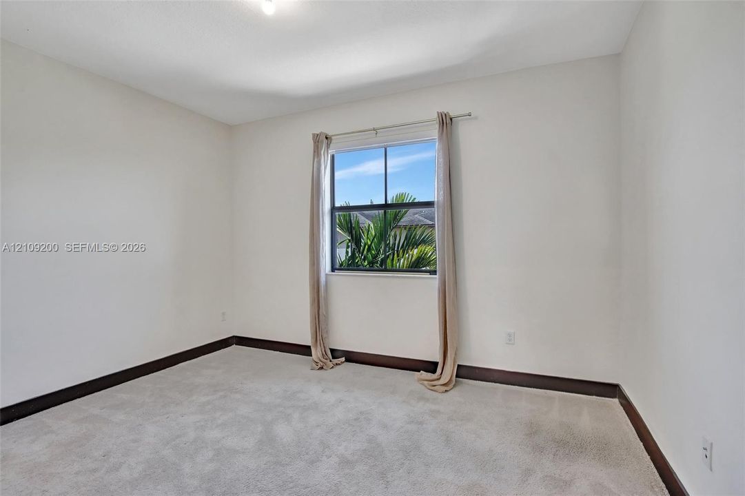 Interior space featuring neutral-toned carpeting, high-contrast dark trim, and a single-pane window with exterior greenery