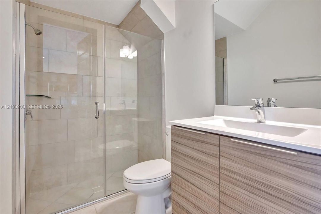 Walk-in shower with floor-to-ceiling tile, frameless glass enclosure, wall-mounted vanity with integrated sink, and large-scale mirror