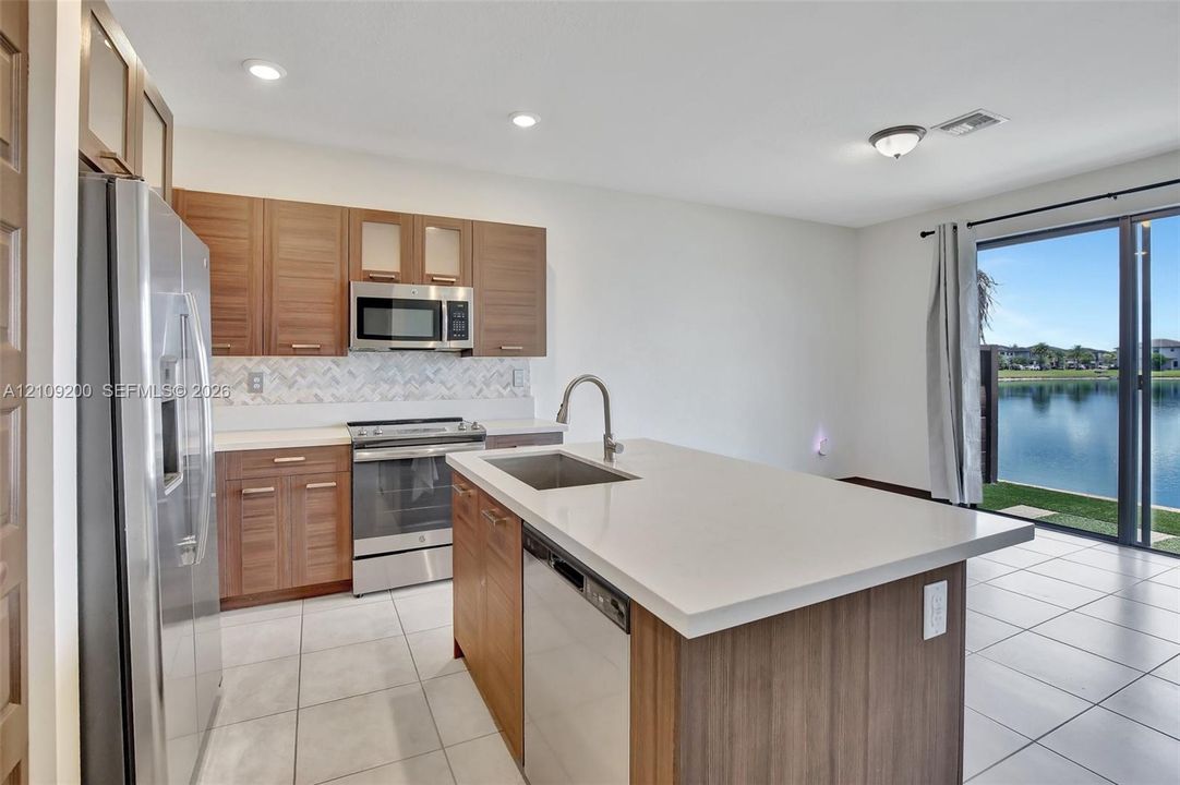 Kitchen featuring flat-panel wood-finish cabinetry, quartz countertops, a herringbone-pattern tile backsplash, stainless steel appliances, and a central island with an undermount sink
