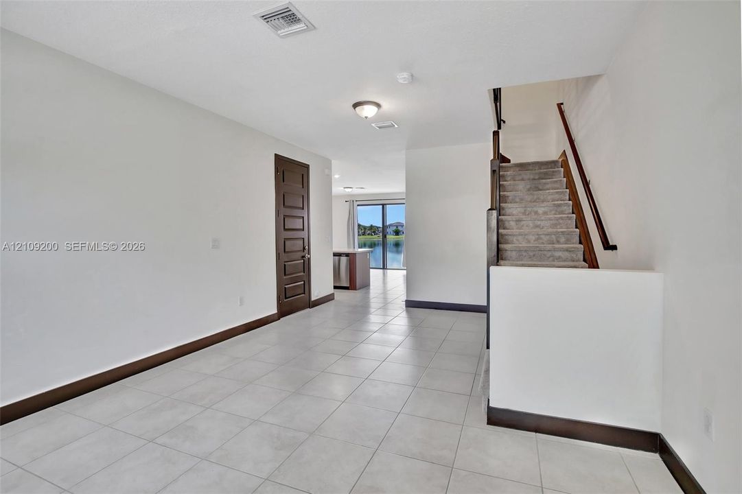 Large-format tile flooring, staircase with a stained wood handrail, and a six-panel solid wood door