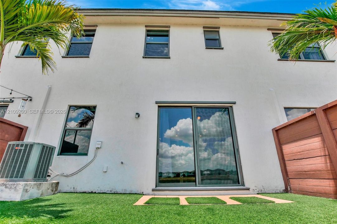 Rear exterior featuring a smooth-stucco facade, sliding glass patio doors, rectangular windows with dark frames, and private wood-style fencing