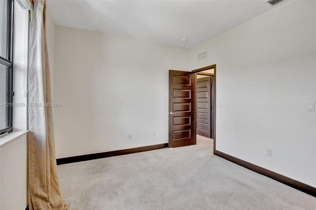 Neutral-toned room featuring carpeting, dark-finish interior doors with five-panel detailing, and a multi-pane window