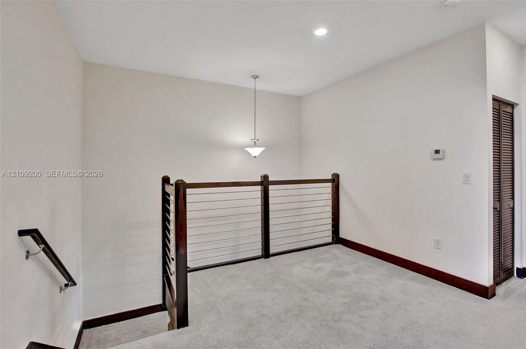 Staircase landing featuring a wood-finish handrail, cable railing system with wood-finish posts, neutral carpeting, and a pendant light fixture