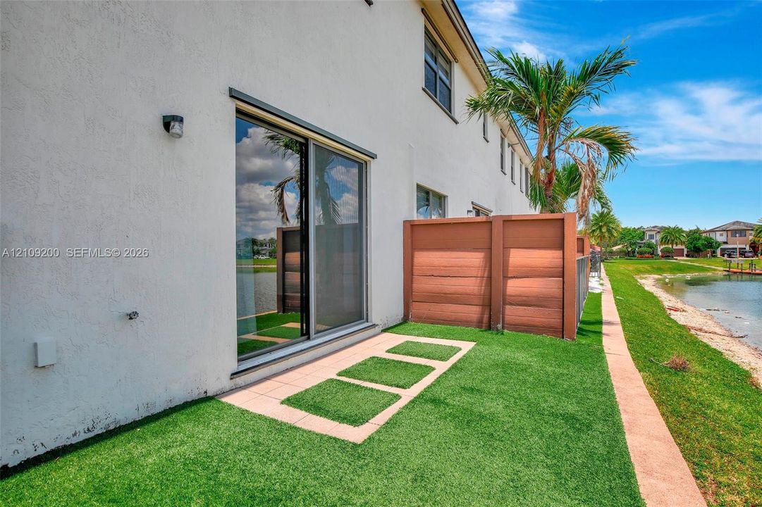 Stucco exterior featuring sliding glass doors, a privacy partition, and a turf patio with paver accents