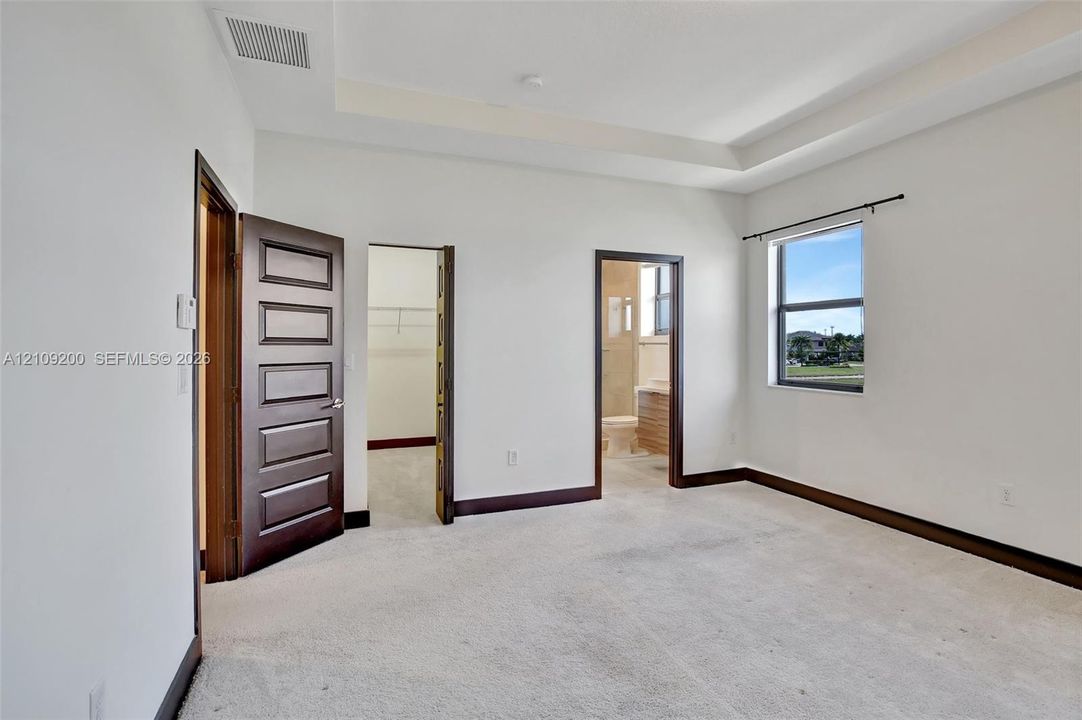 Room featuring a tray ceiling, neutral carpeting, dark wood-finish door frames, and single-pane window