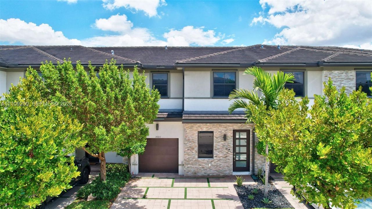 Two-story exterior featuring a stone veneer facade, a tiled roof, a multi-pane glass entry door, and a paver driveway with turf accents