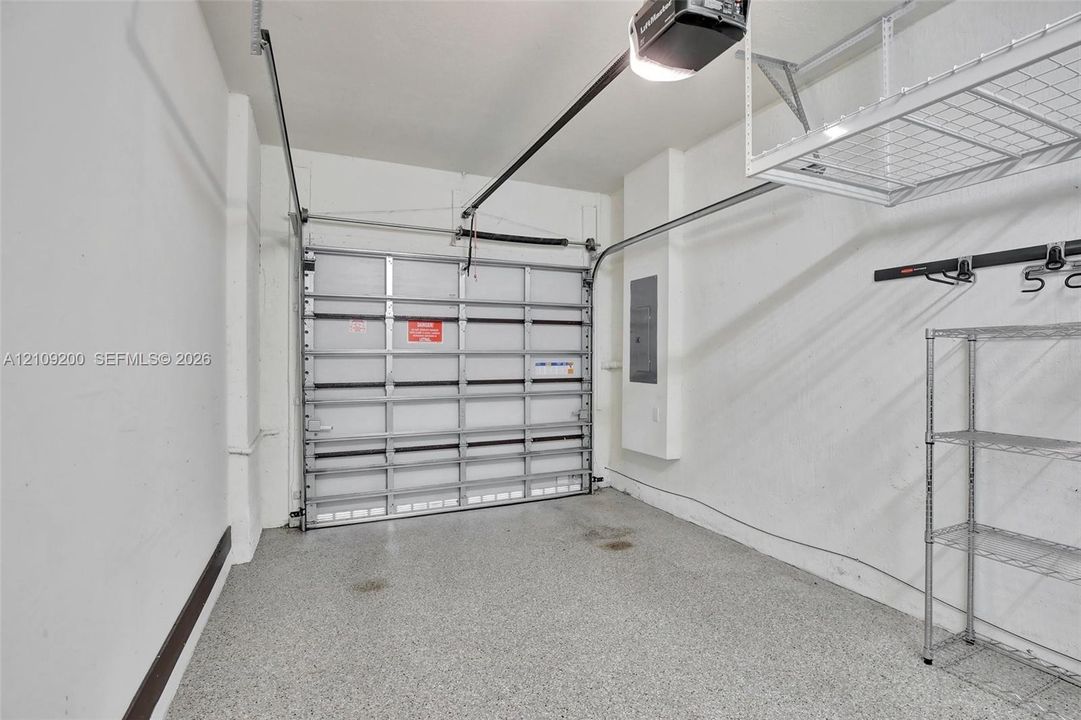 Garage featuring speckled epoxy flooring, sectional metal garage door, ceiling-mounted storage rack, and wall-mounted electrical panel