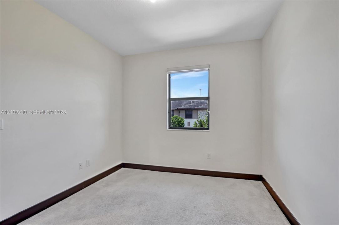 Neutral-toned room featuring plush wall-to-wall carpeting, crisp white walls, and a single-pane window with a roller shade