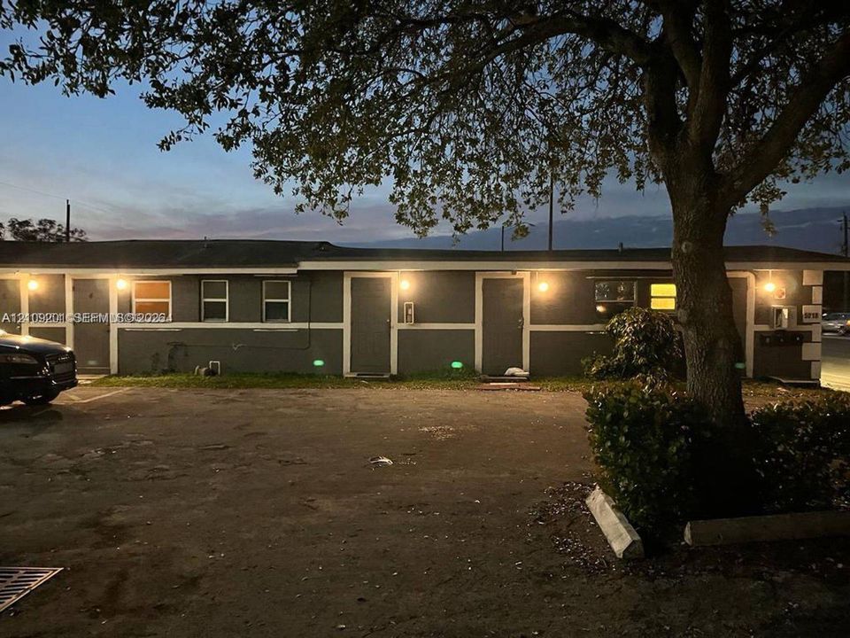 Single-story exterior featuring a dark grey finish, paved parking area, and mature canopy tree
