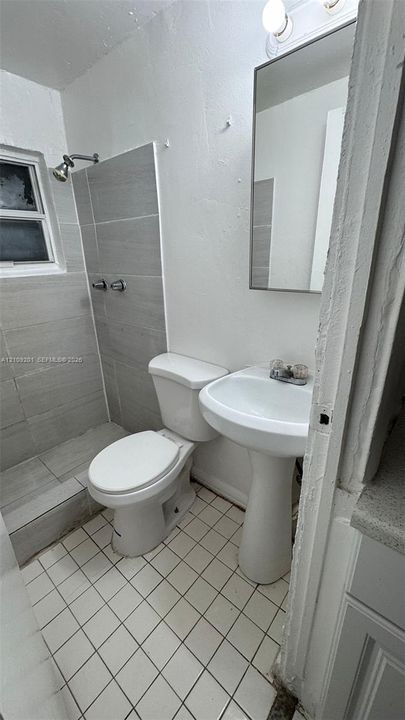 Bathroom featuring a walk-in shower with grey horizontal tiling, white pedestal sink, tiled flooring, and a wall-mounted rectangular mirror