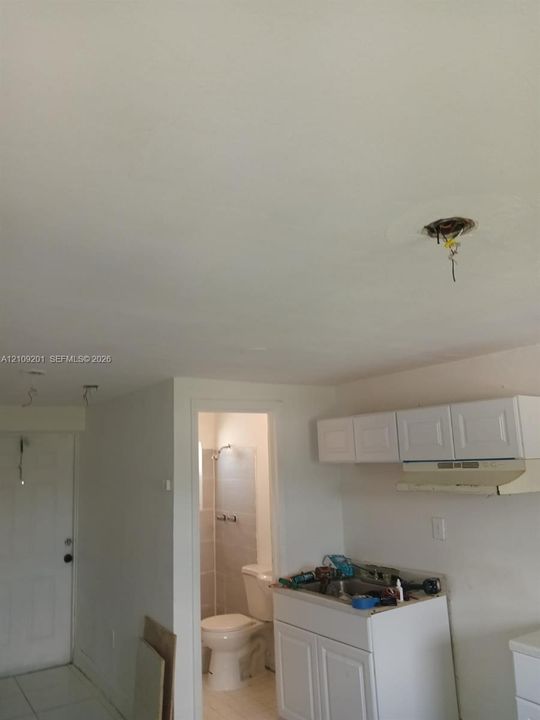White cabinetry featuring shaker-style doors, integrated range hood, tile flooring, and standard-height plumbing fixtures