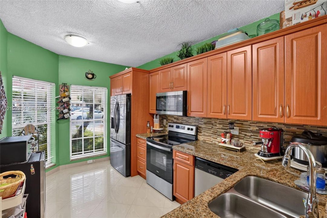 Kitchen featuring stained wood cabinetry, stone countertops, a mosaic tile backsplash, stainless steel appliances, and tile flooring