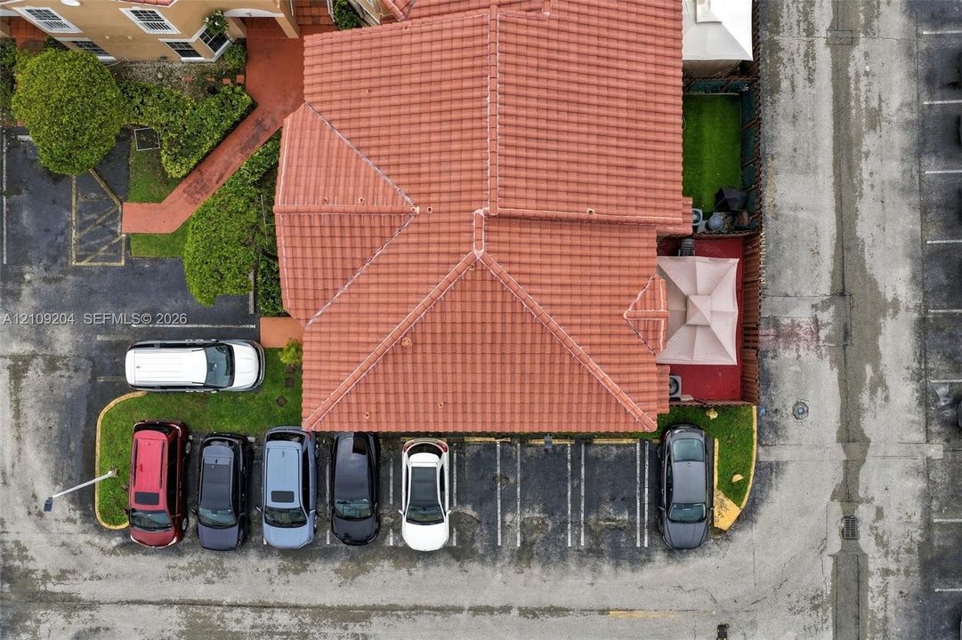 Aerial view featuring a terracotta tile roof, designated asphalt parking spaces, and manicured turf landscaping