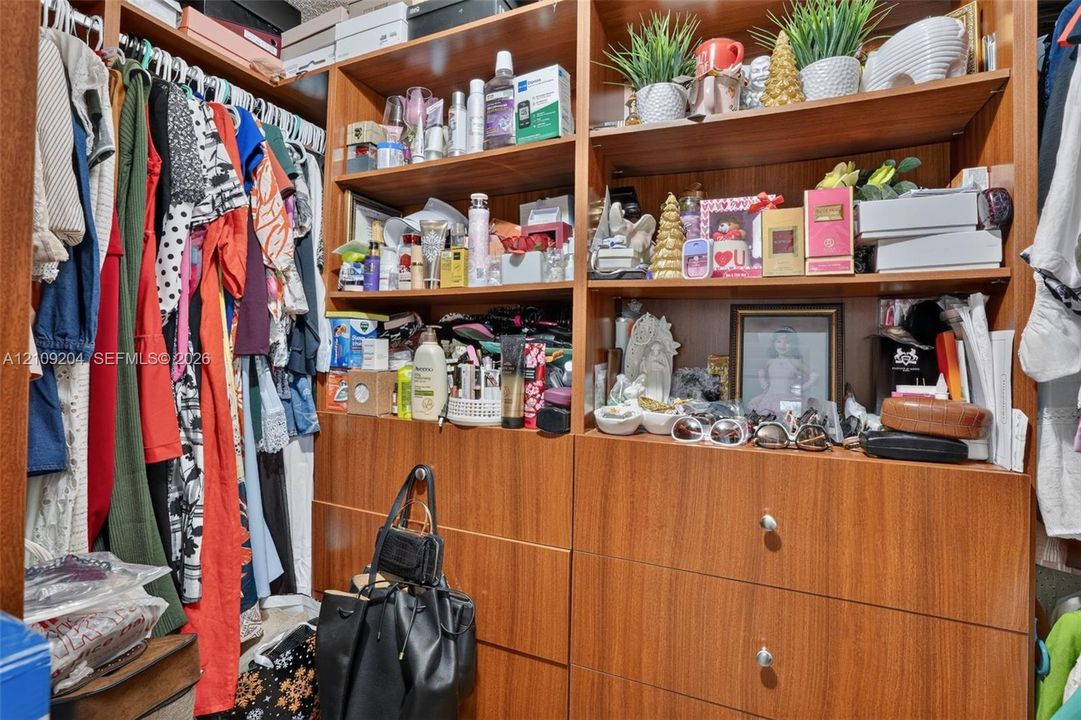 Custom closet system featuring floor-to-ceiling wood-finish cabinetry, built-in shelving, integrated dresser drawers with round hardware, and dual hanging rods