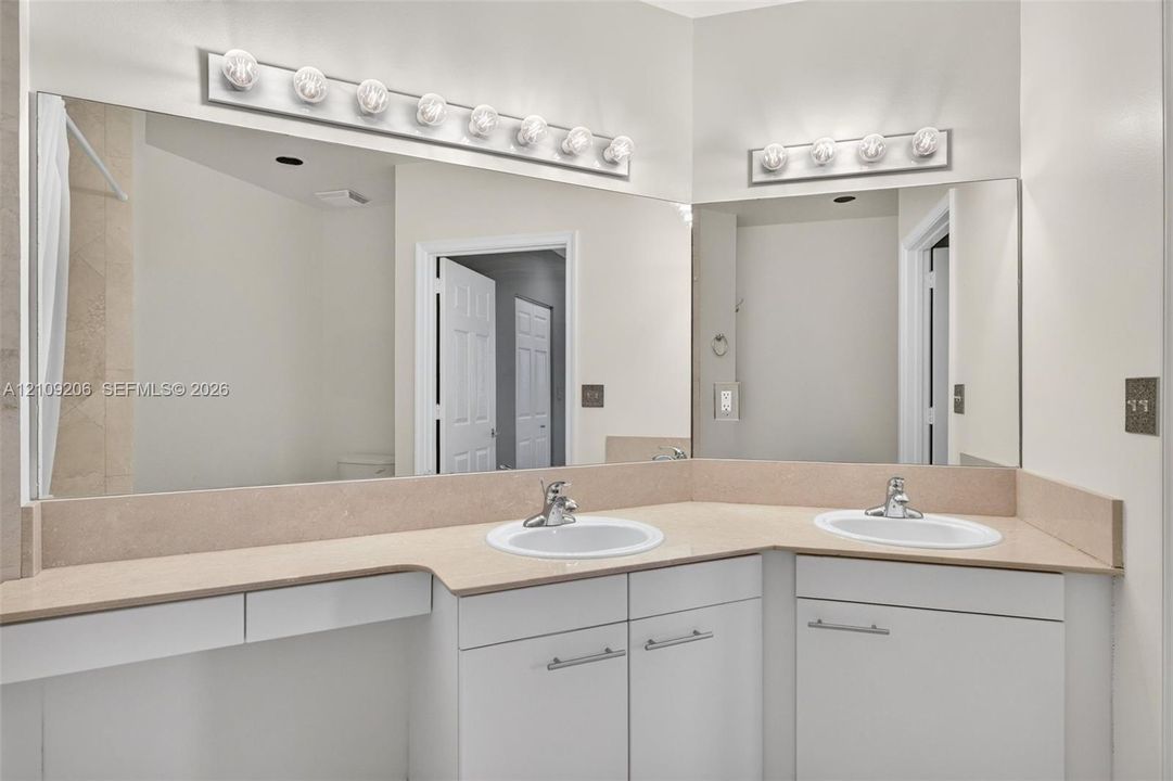 Dual-basin vanity featuring white cabinetry, solid-surface countertop, integrated backsplashes, and wall-mounted light fixtures