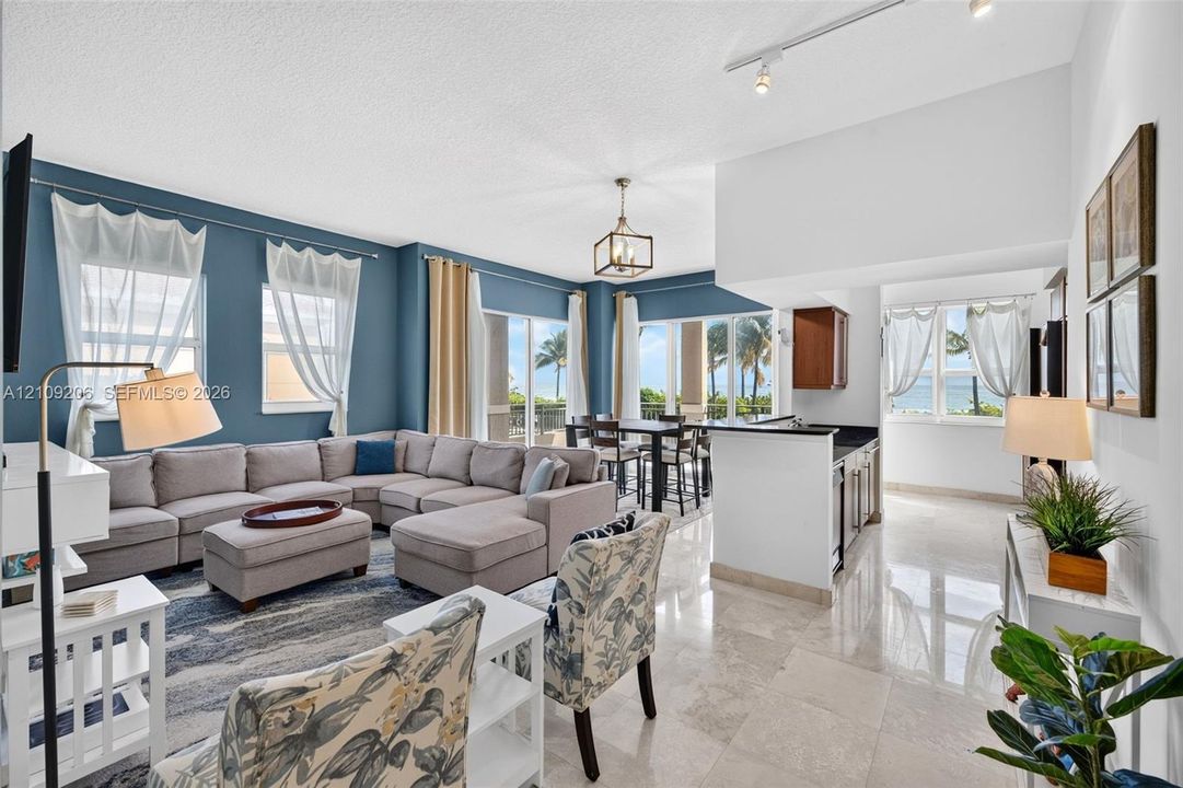 Open-concept interior featuring light-toned stone tile flooring, high ceilings with track and pendant lighting, and floor-to-ceiling glass sliding doors