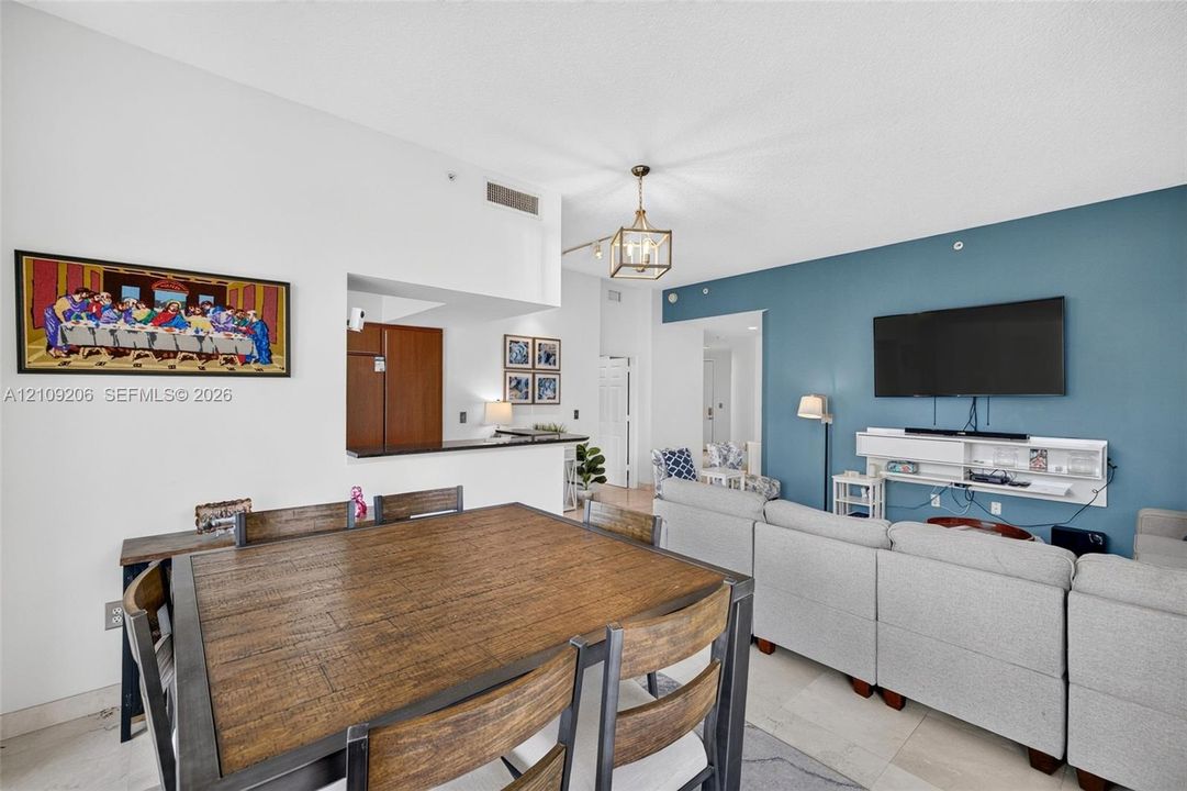 Open-concept interior featuring a high ceiling, accent wall, polished tile flooring, pendant lighting, and a breakfast bar