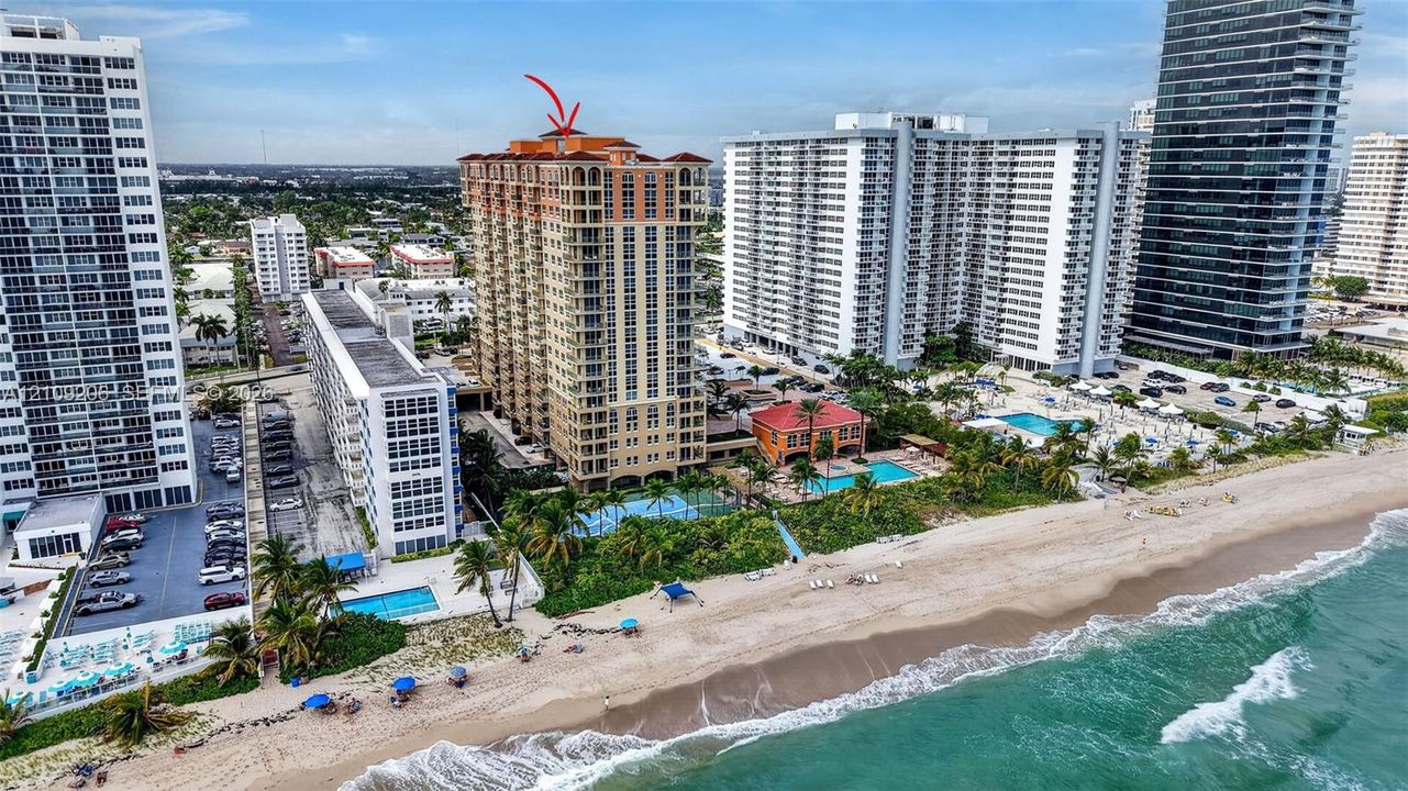 High-rise residential building featuring stucco exterior, arched window detailing, terracotta tile roofing, and direct beach access