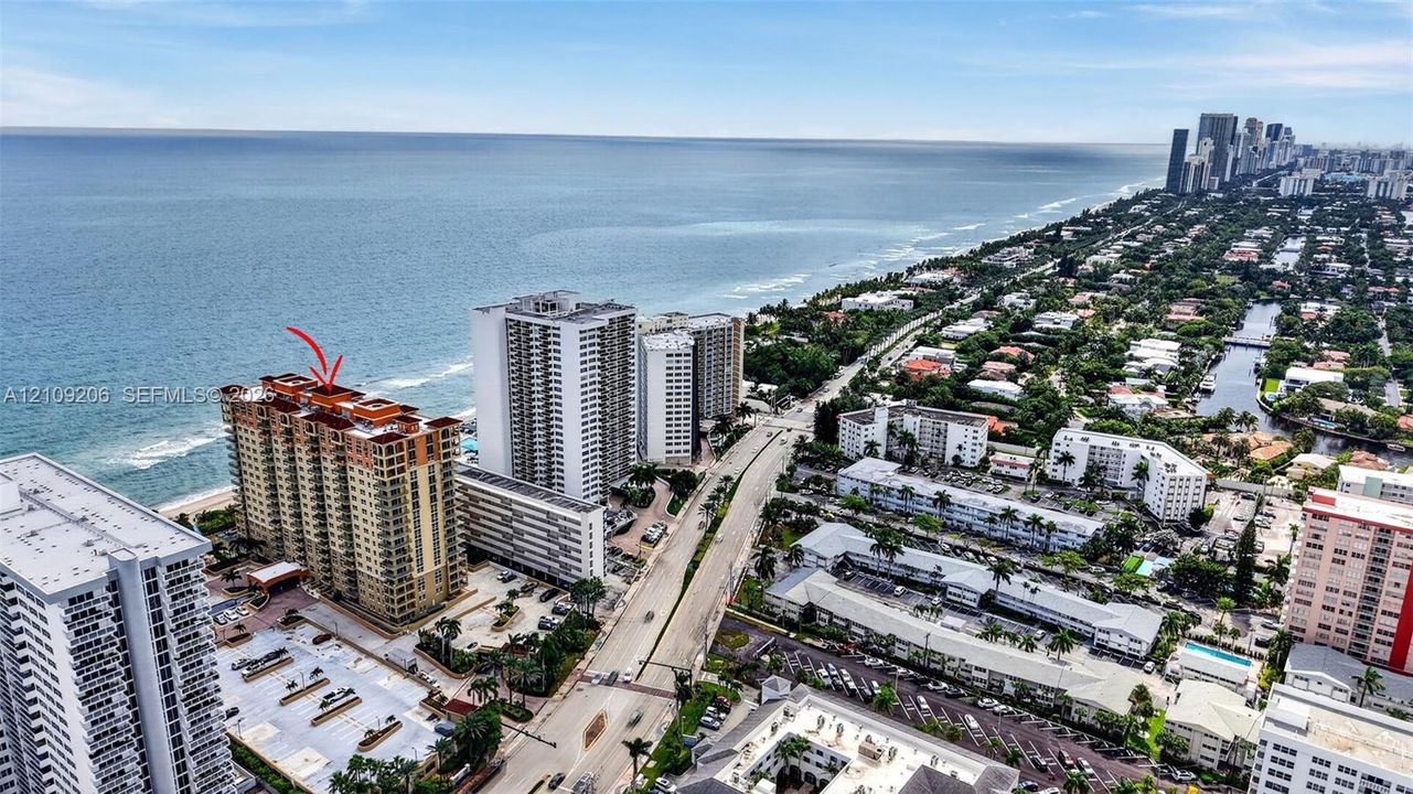 High-rise coastal building featuring a terracotta-tiled roof, private balconies, and immediate proximity to the oceanfront