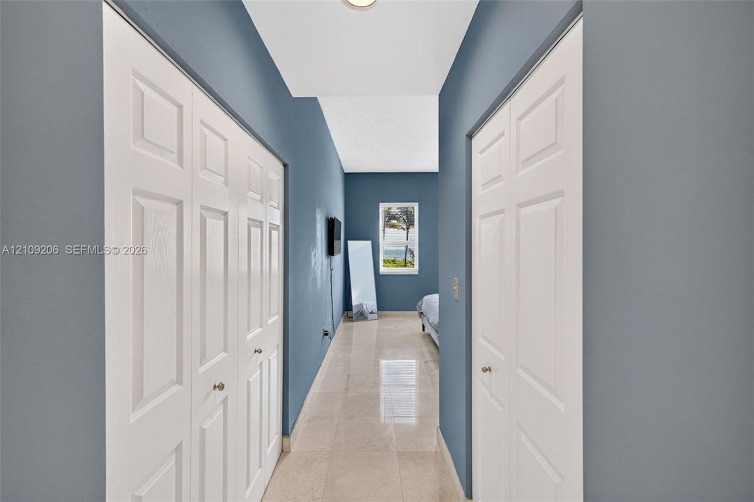 Hallway featuring polished tile flooring, dual six-panel bifold closet doors, and a single window with exterior scenery