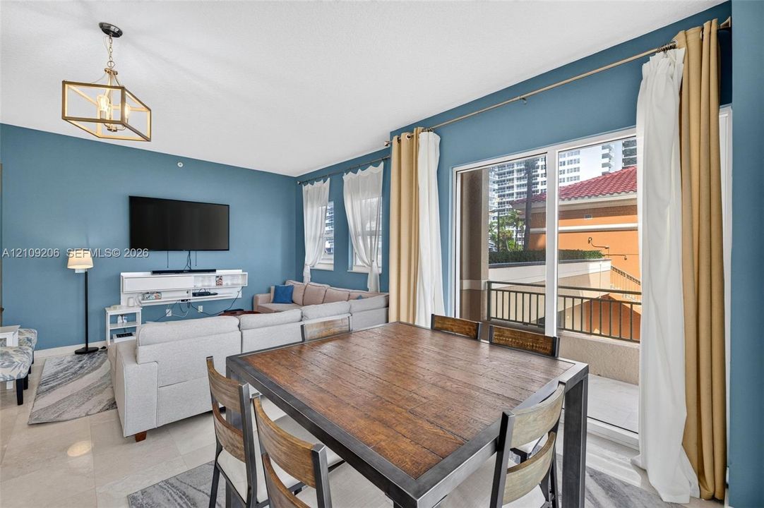 Large-format sliding glass doors, geometric metal-frame chandelier, expansive tile flooring, and private balcony with metal railing