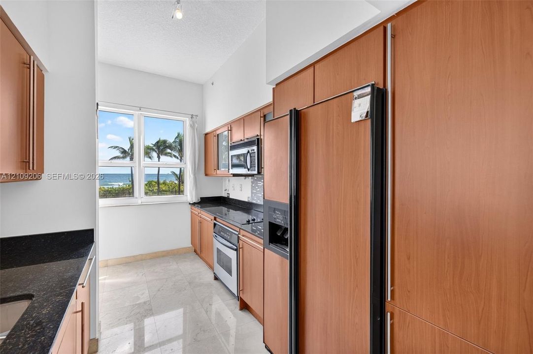 Kitchen featuring wood-veneer cabinetry, dark stone countertops, tile flooring, and stainless steel appliances with an ocean horizon backdrop
