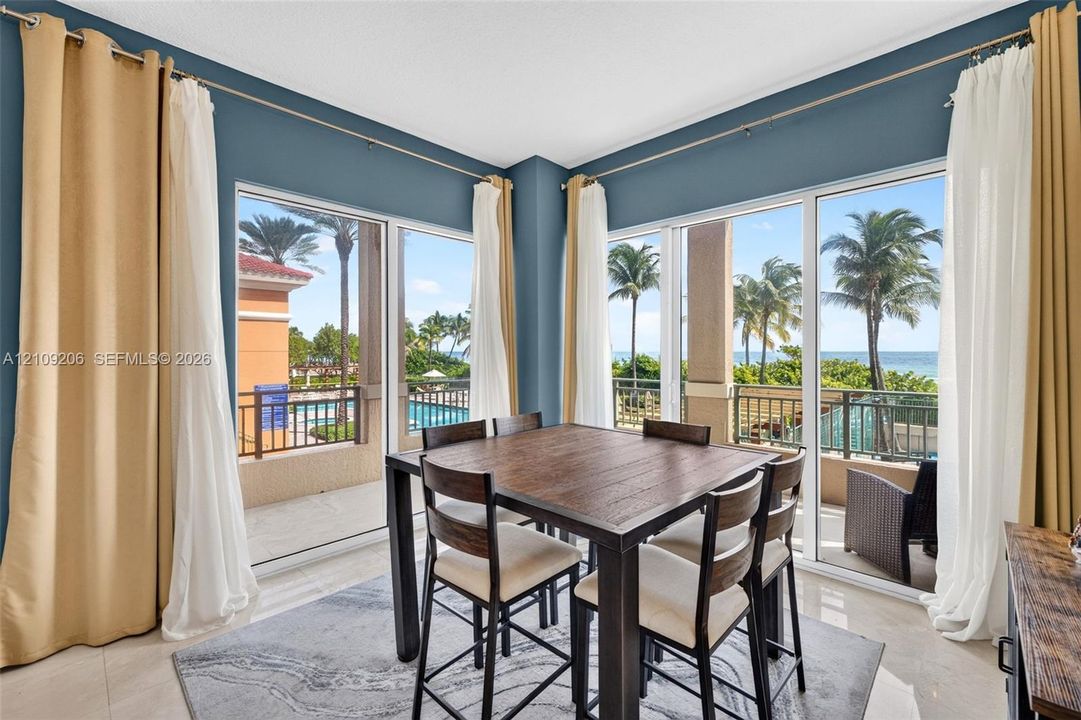Corner dining space featuring floor-to-ceiling glass sliding doors, neutral tile flooring, and coastal water backdrop
