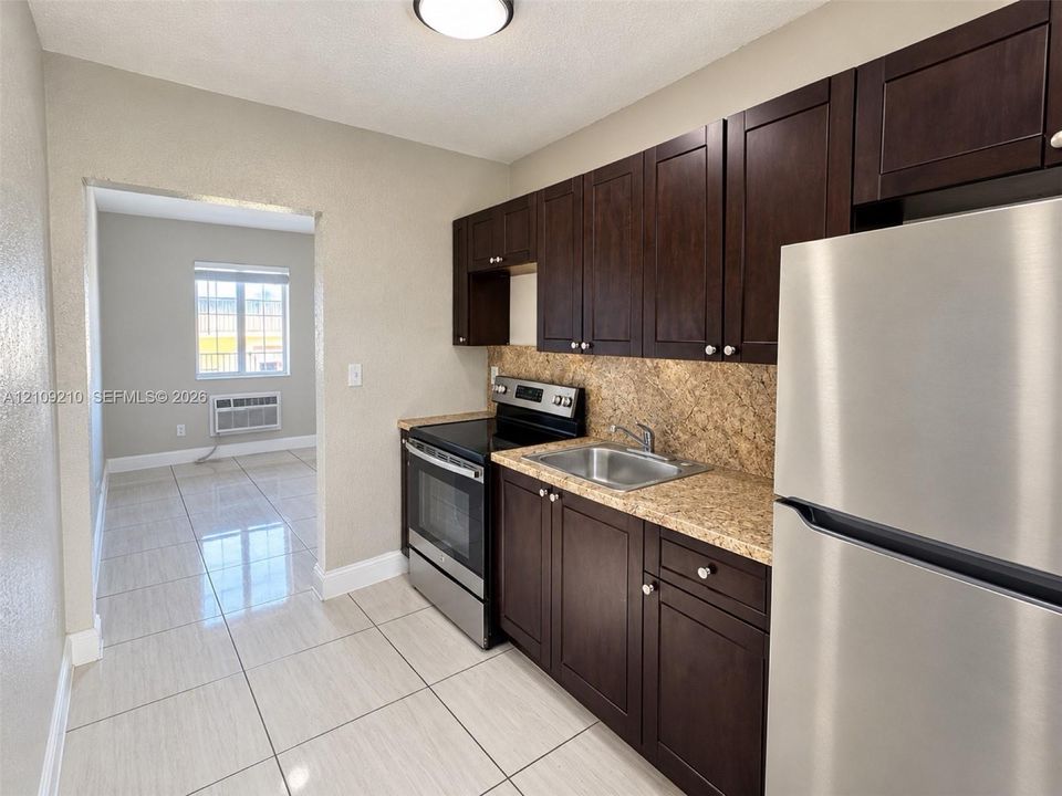 Kitchen featuring espresso-toned cabinetry, stone-finish countertops, stainless steel appliances, and large-format tile flooring