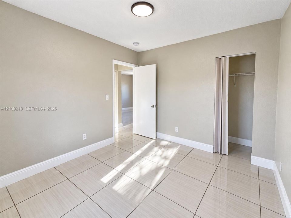 Neutral-toned room featuring large-format tile flooring, a mounted flush-mount ceiling light, and a closet with a bi-fold door