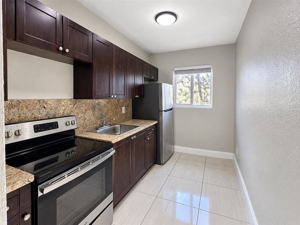 Kitchen featuring dark wood-finish cabinetry, stone-texture countertops, stainless steel appliances, and large-format tile flooring