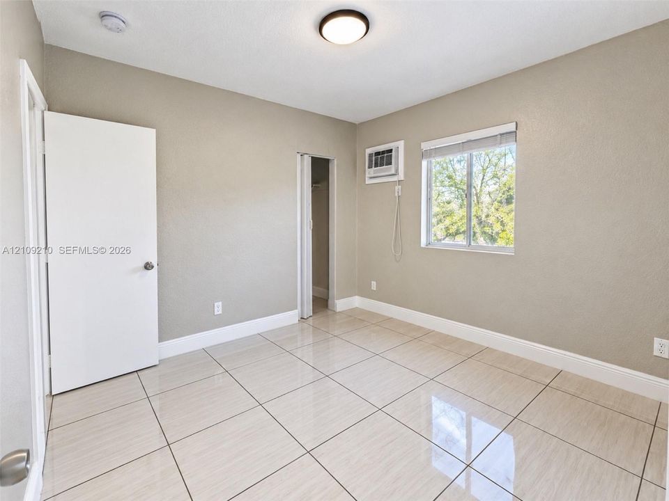 Neutral-toned interior featuring large-format tile flooring, dual-pane window, built-in wall-mounted cooling unit, and solid-core interior doors