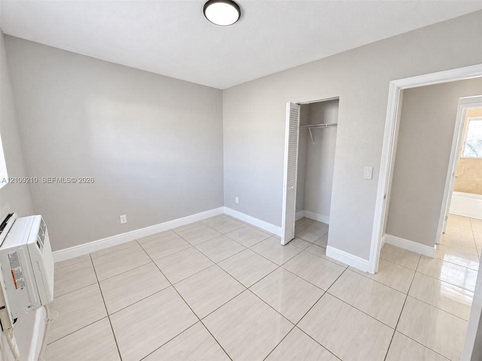 Neutral-toned room featuring ceramic tile flooring, a built-in closet with louvered doors, and a wall-mounted cooling unit