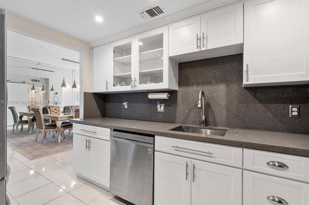 Kitchen featuring white shaker-style cabinetry, glass-front upper cabinet doors, dark-toned solid surface countertops, a stainless steel under-mount sink, and a stainless steel dishwasher