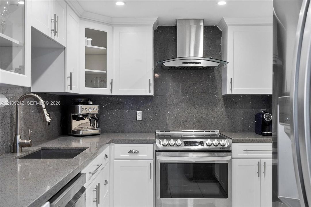 Kitchen featuring white shaker-style cabinetry, dark stone-finish countertops, full-height matching backsplash, stainless steel range with overhead chimney hood, and undermount sink with pull-down faucet