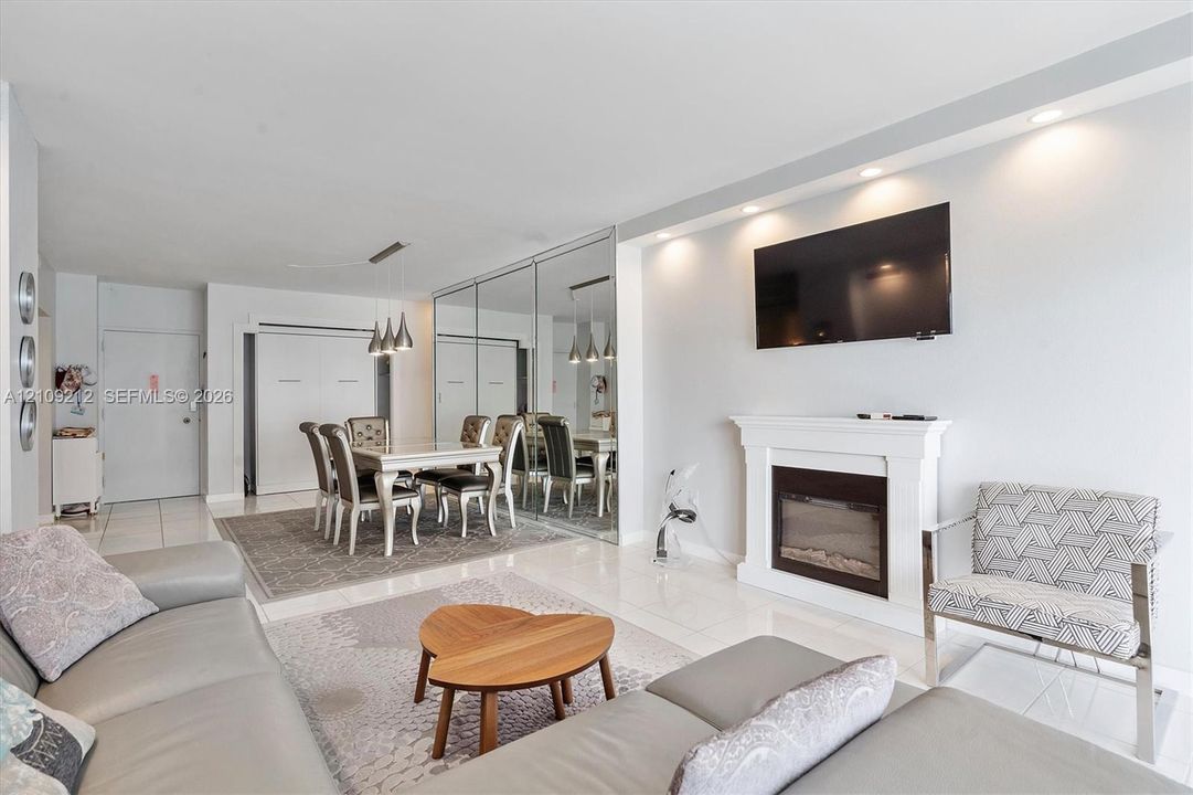 Living area featuring a fireplace with a white mantel, recessed ceiling lighting, mirrored wall accents, and light-toned tile flooring