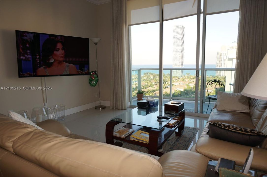 Floor-to-ceiling windows, ceramic tile flooring, and sliding glass doors opening to a balcony with water and skyline scenery