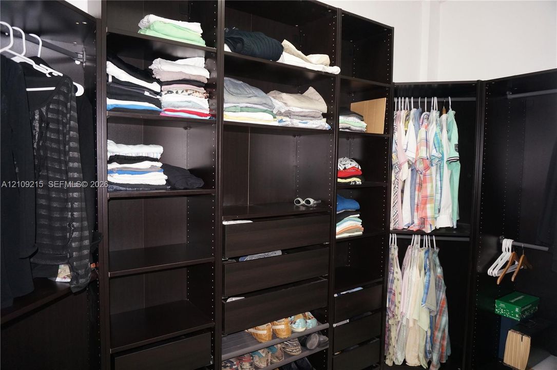 Built-in floor-to-ceiling storage system featuring a dark wood-finish, adjustable open shelving, multiple integrated drawers, and dual-level hanging rods